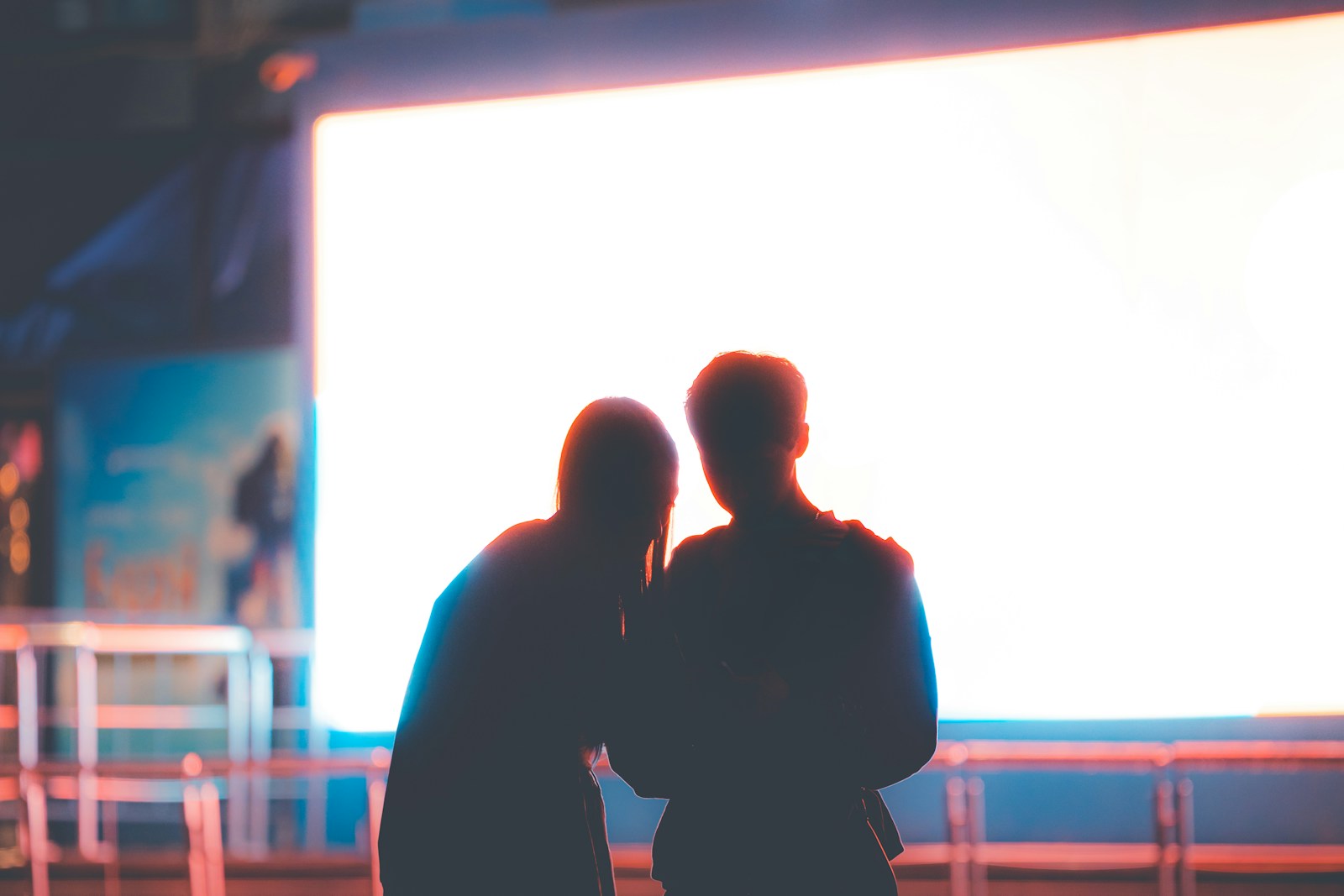 Two people stand close together, silhouetted against a glowing cinema screen